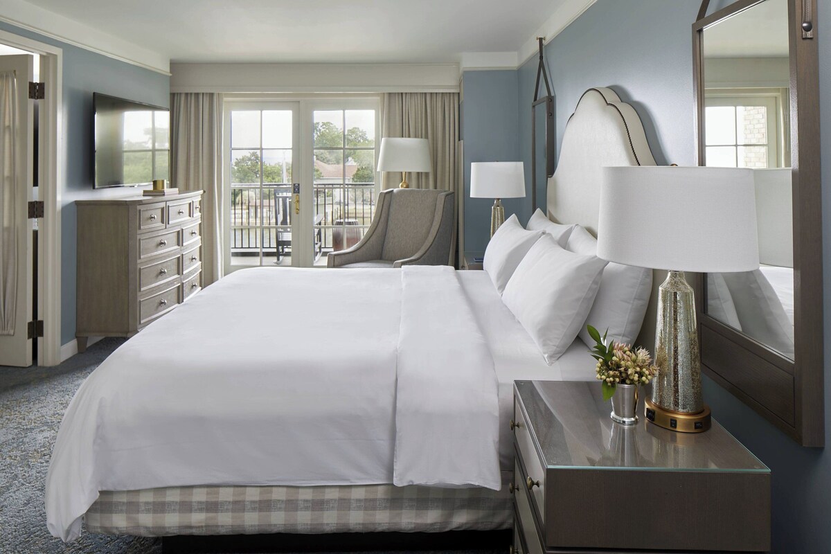 A hotel room with a large bed, a desk with a lamp, a chair, a dresser, and a television.