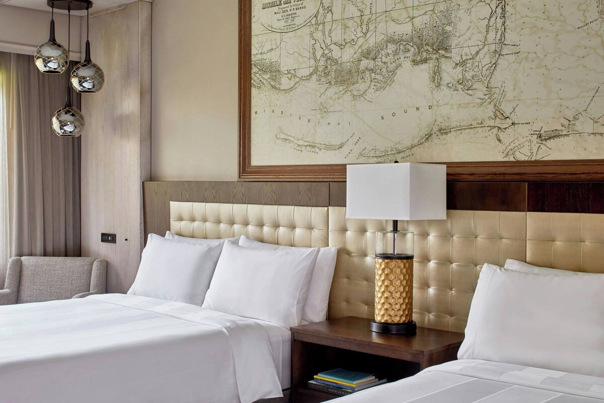 Une chambre d’hôtel avec une grande carte accrochée au mur, un lit recouvert de draps blancs, une table de chevet avec une lampe et une chaise.