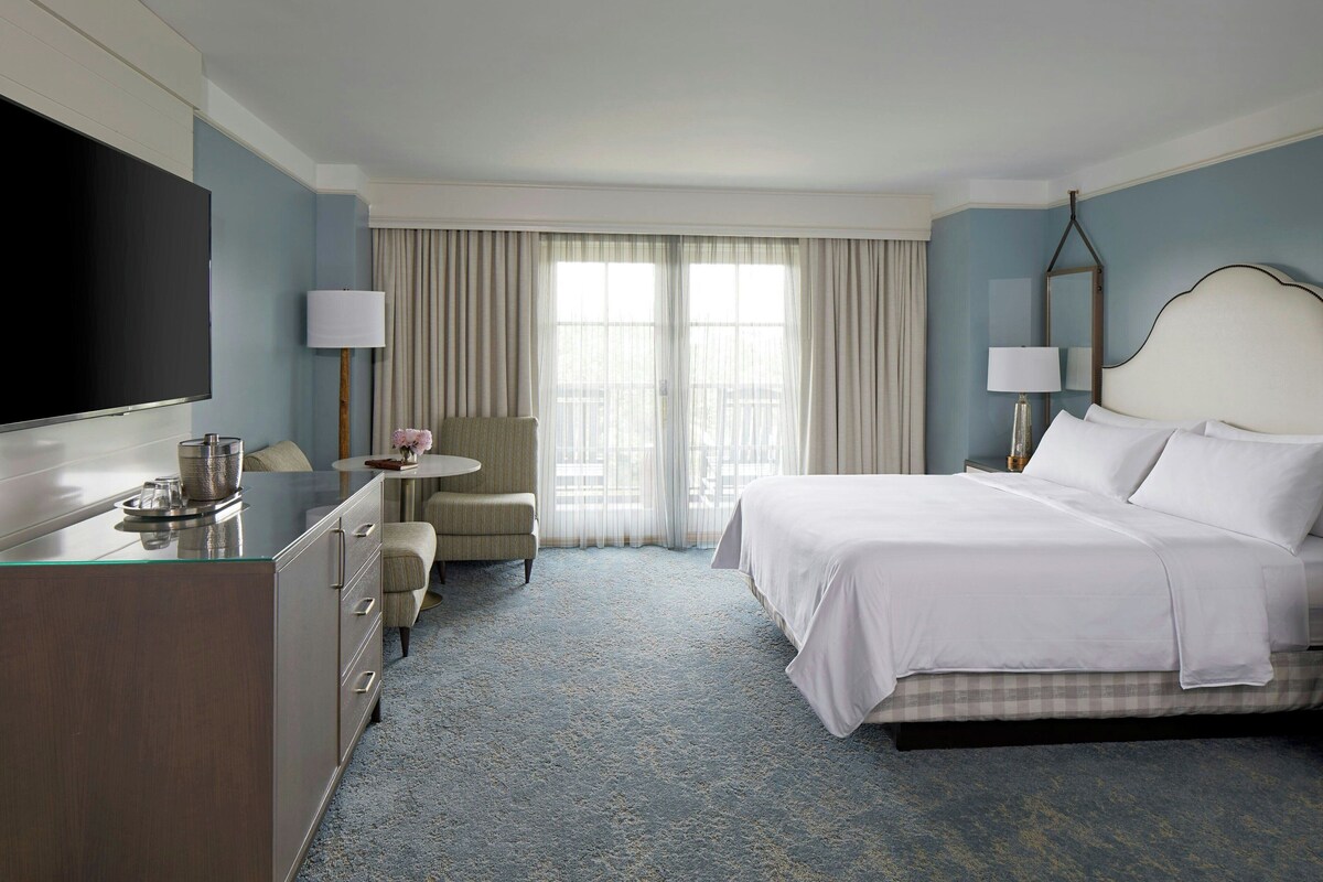 A hotel room with a bed, a desk, a chair, a TV, and a window with curtains.