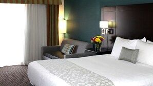 Een hotelkamer met een groot bed, een bank, een nachtkastje met een lamp en een bloemenvaas.