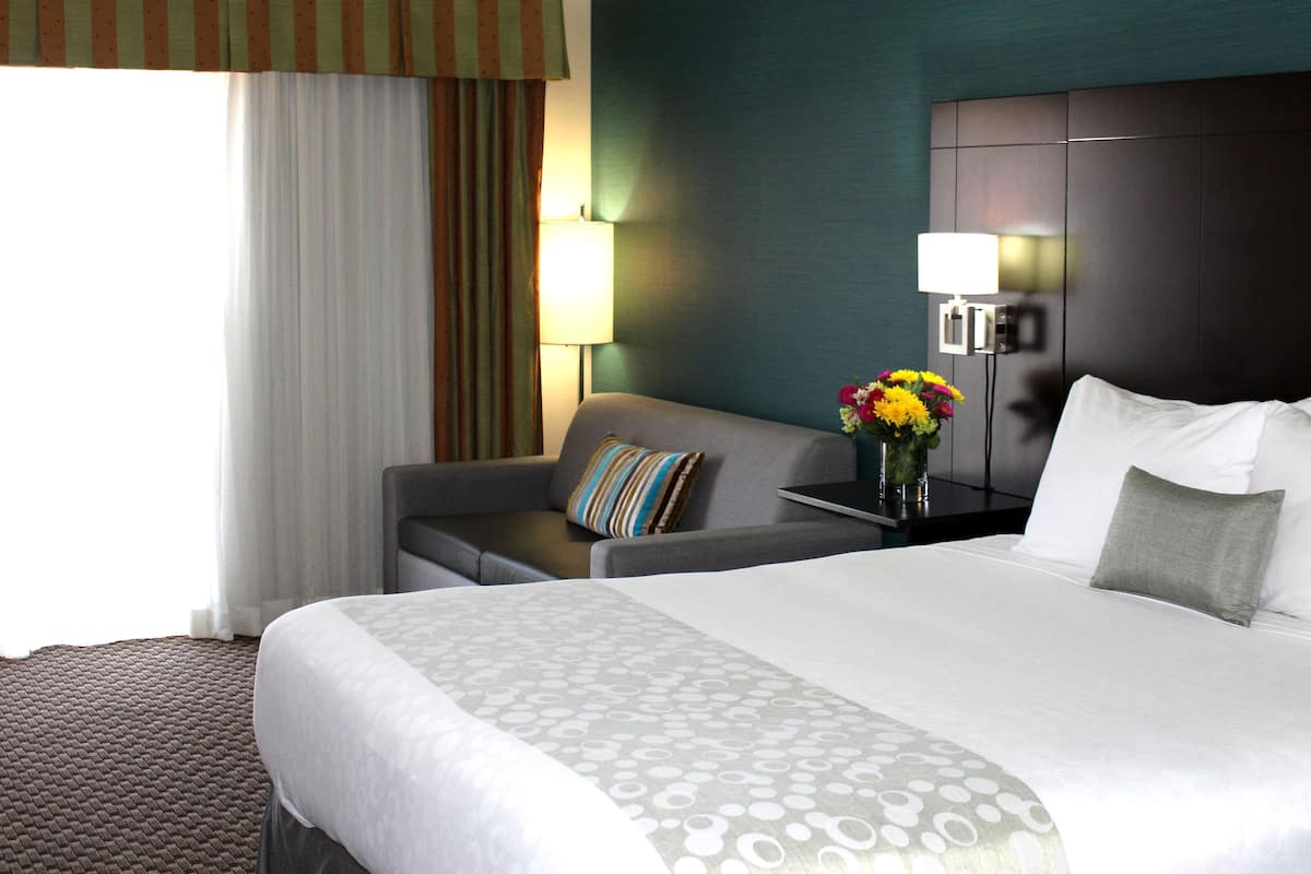 A hotel room with a large bed, a sofa, a nightstand with a lamp, and a vase of flowers.
