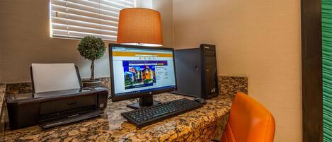 A desktop computer with a monitor, keyboard, and a printer on a granite countertop. There is a potted plant and a window with blinds in the background.