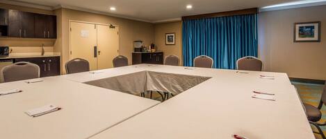 A conference room with a long table, chairs, a kitchenette, and a blue curtain.