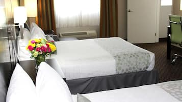 A hotel room with two beds, a desk with a lamp, a chair, and a window with curtains.