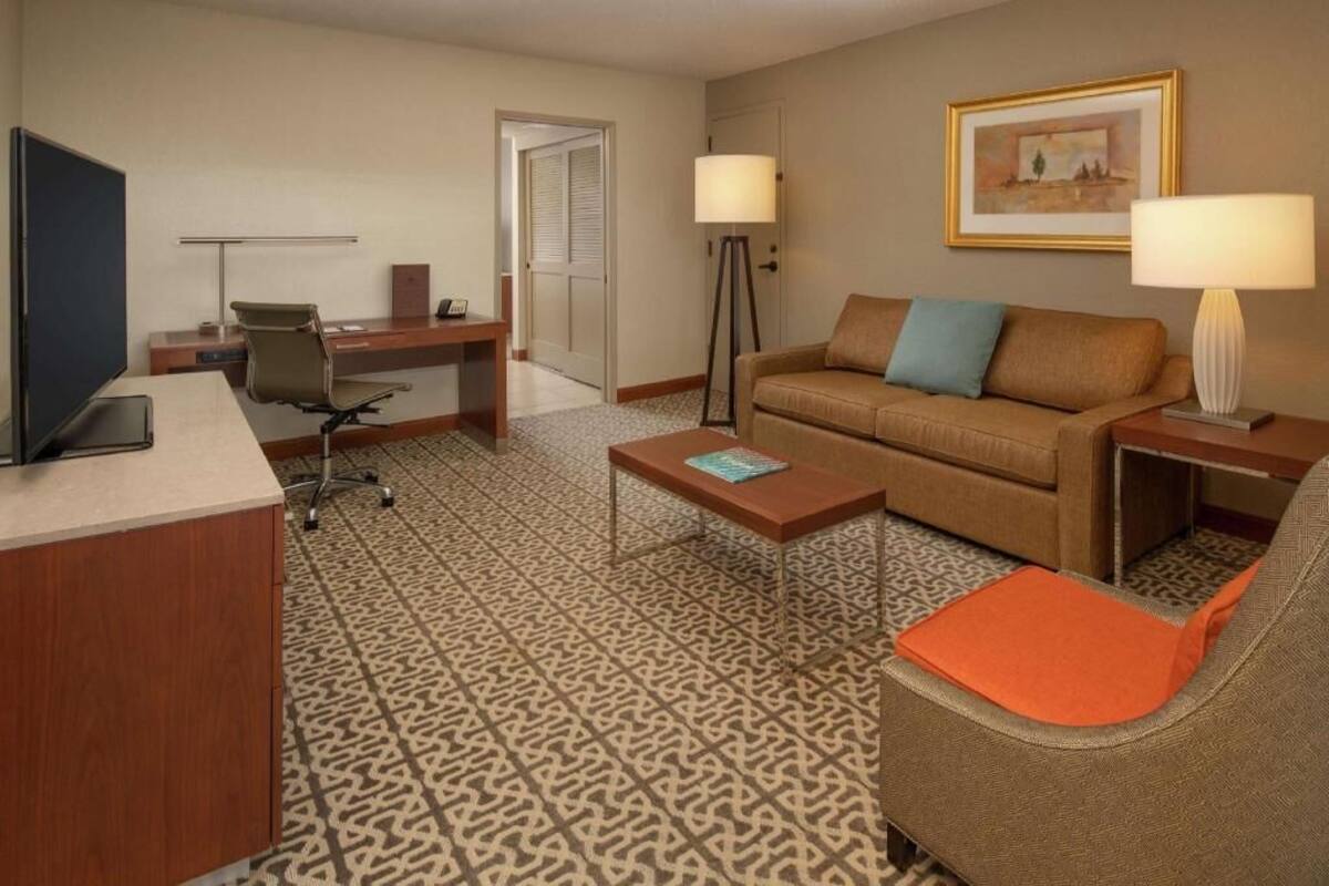 Habitación de hotel con escritorio, sofá, mesa de centro, televisor y lámpara.