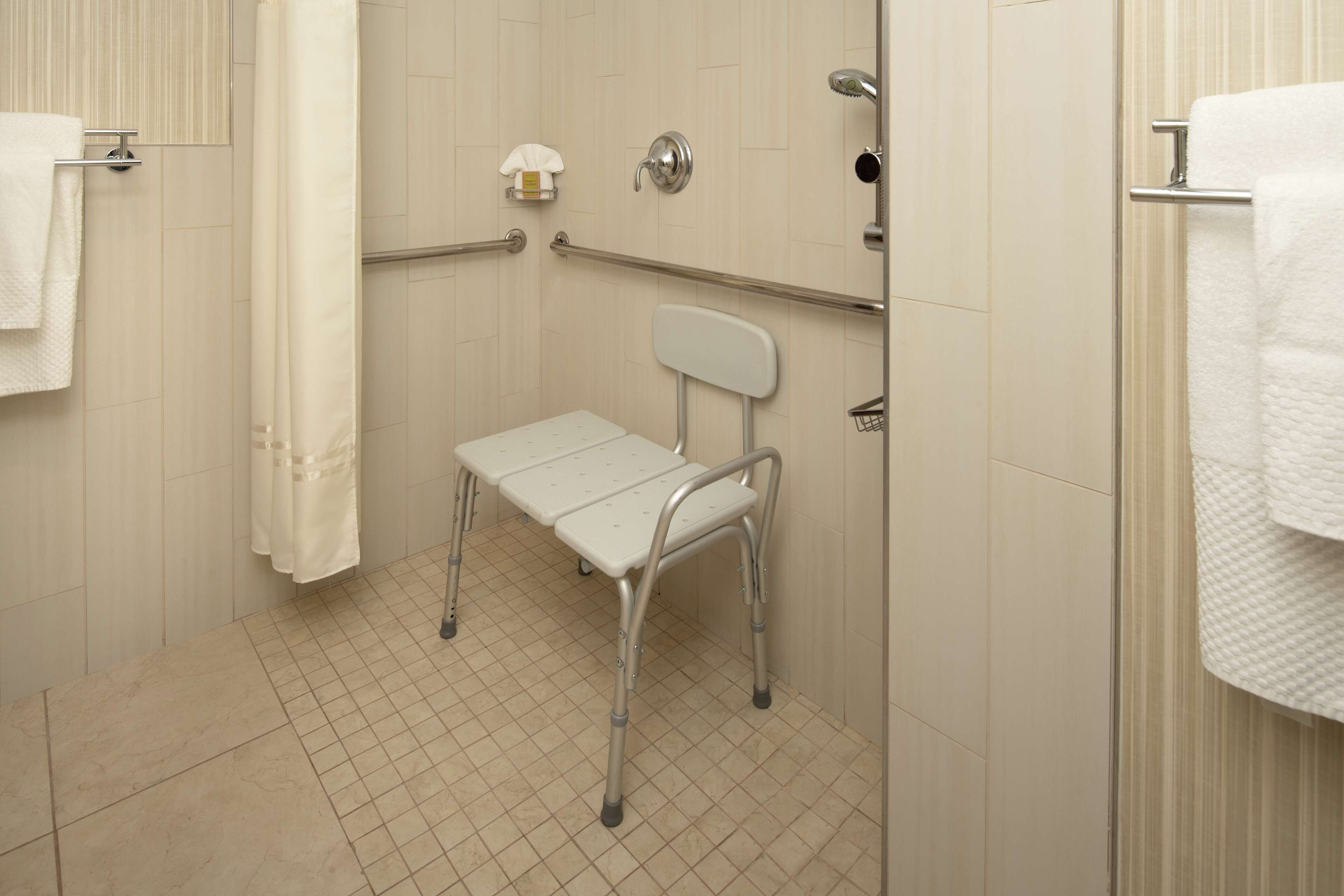 A bathroom with a white tiled floor, a white shower curtain, a white towel rack, a white toilet, and a white grab bar.