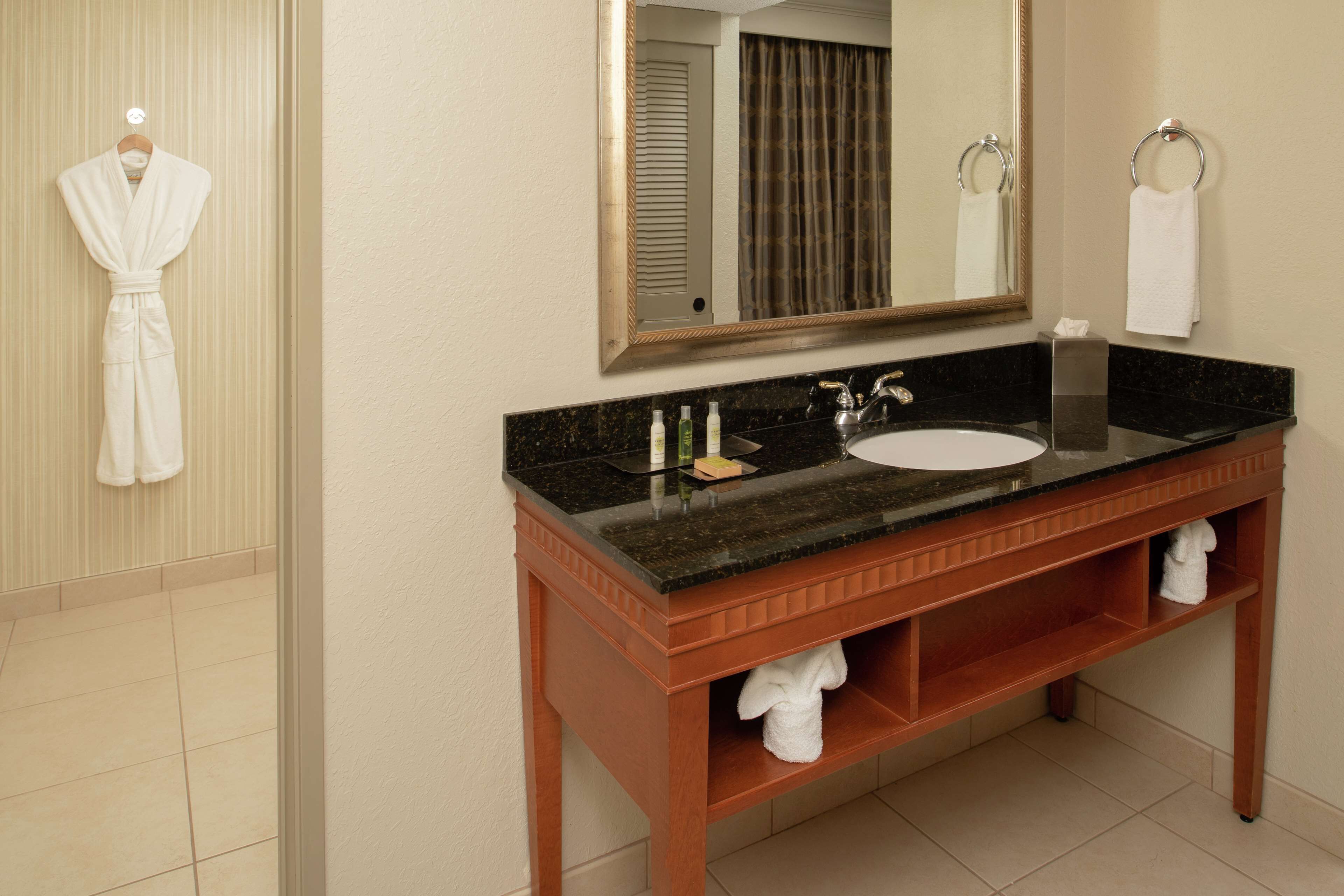 A bathroom with a wooden vanity, a sink, and a mirror. There are towels hanging on the wall and a robe on a hook.