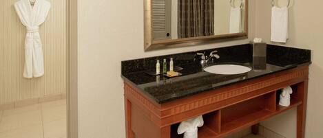 A bathroom with a wooden vanity, a sink, and a mirror. There are towels hanging on the wall and a robe on a hook.
