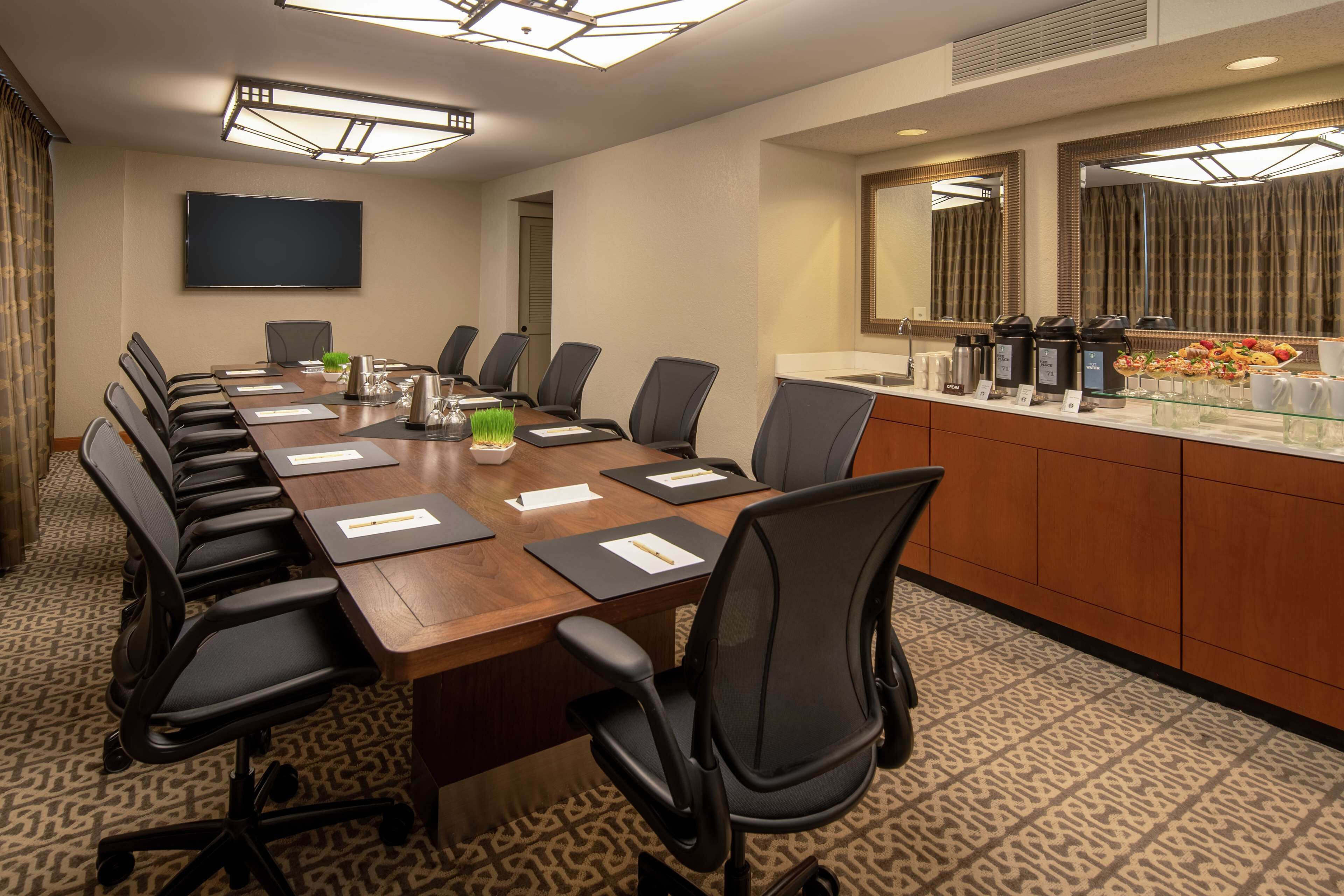 A conference room with a long table, chairs, a TV, and a buffet area with food and beverages.