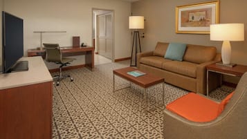 A hotel room with a desk, a television, a sofa, a coffee table, and a floor lamp.