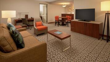 A hotel room with a sofa, a coffee table, a TV, a desk, and a dining area.