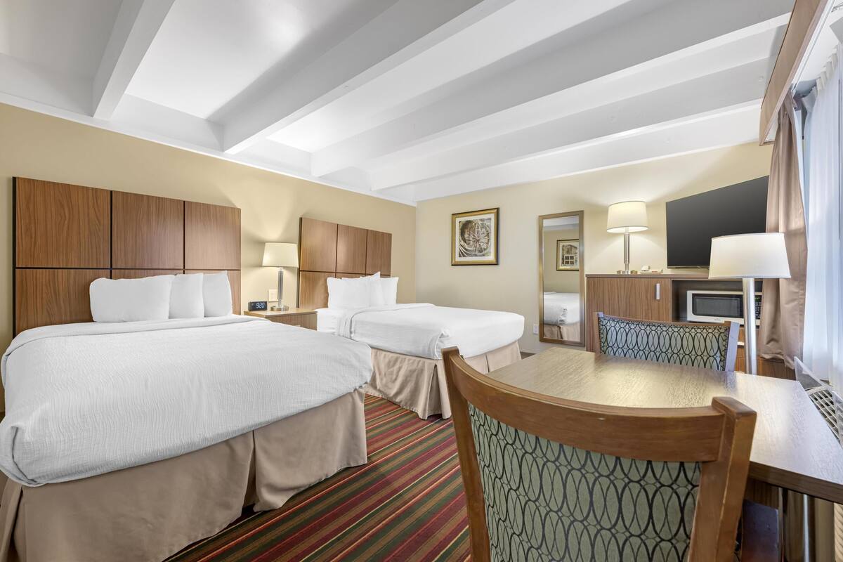 A hotel room with two beds, a dining table, a TV, and a desk with a lamp.