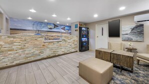 A reception area with a stone wall, a digital kiosk, a seating area with a sofa and a small table, and a mural depicting a desert landscape. - Best Western El Rancho Palacio (Roswell)