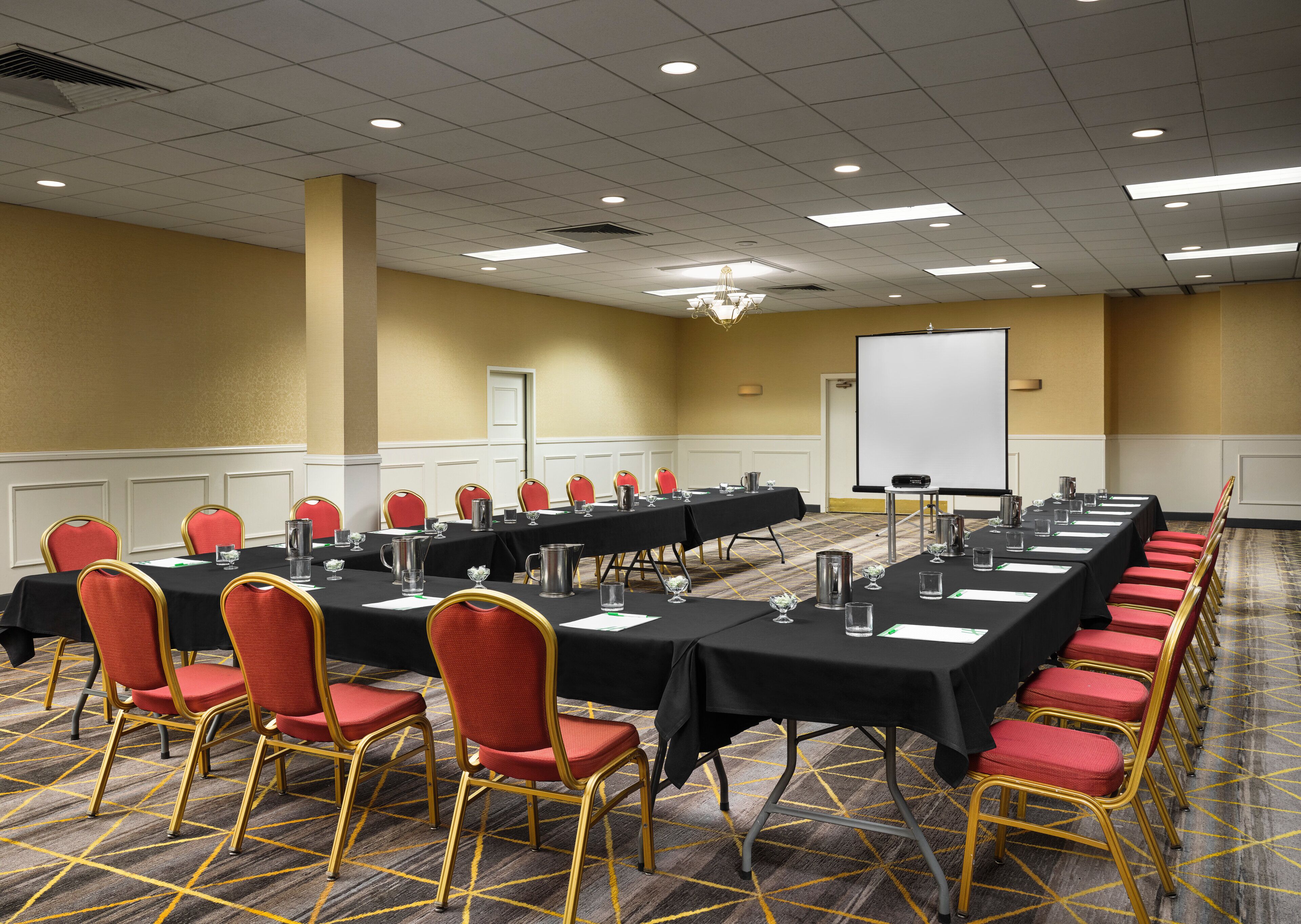 A conference room with long tables, red chairs, and a projector screen.