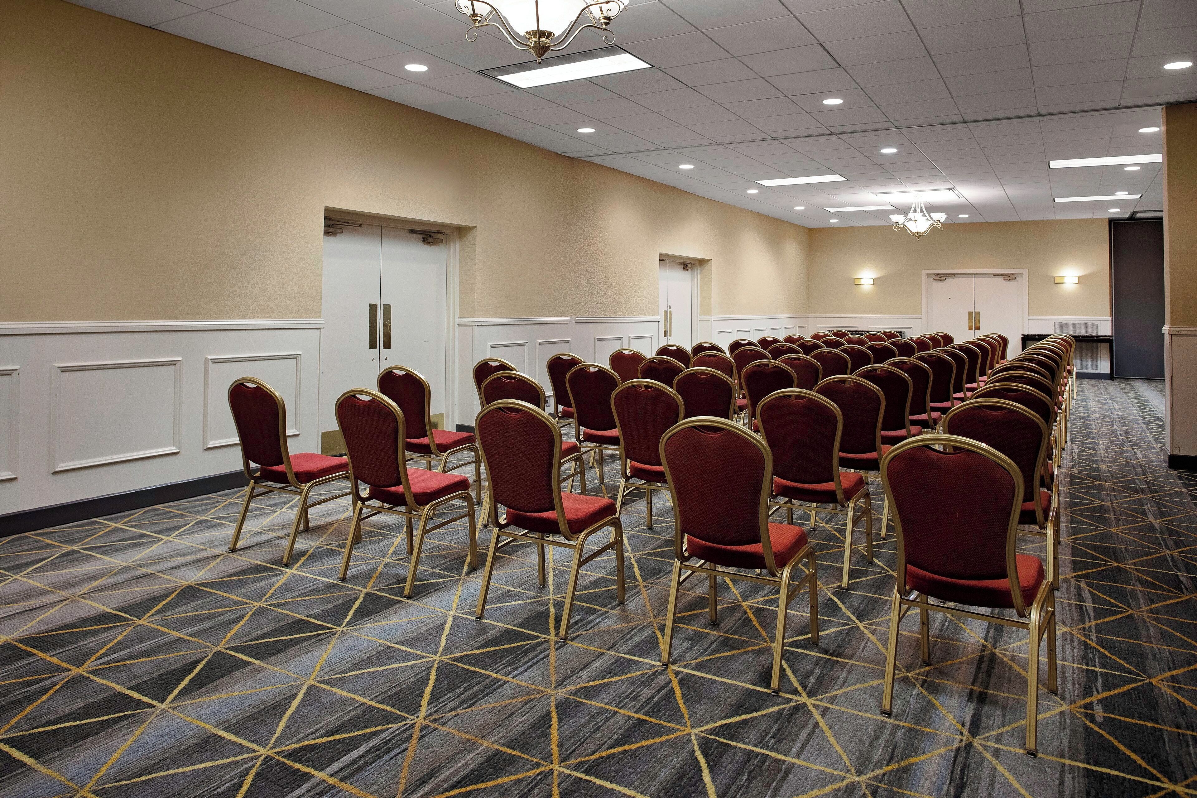 A conference room with rows of red chairs and a patterned carpet.