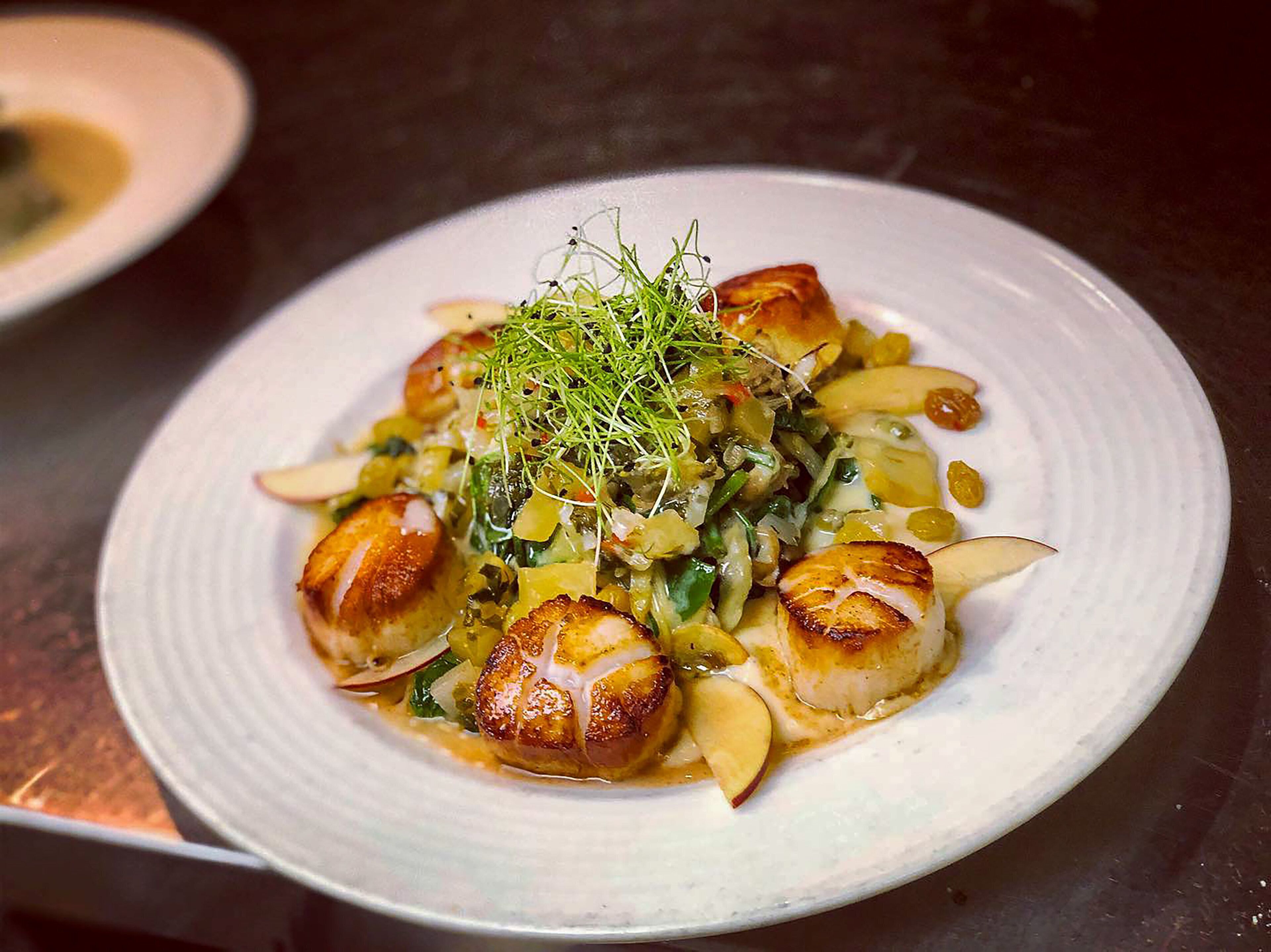 Un plato de vieiras salteadas, adornado con hierbas verdes y lonchas de manzana.