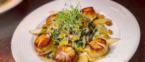 Un plato de vieiras salteadas, adornado con hierbas verdes y lonchas de manzana.