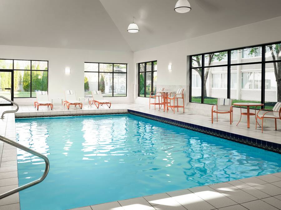 An indoor swimming pool with clear blue water, surrounded by white walls and large windows.