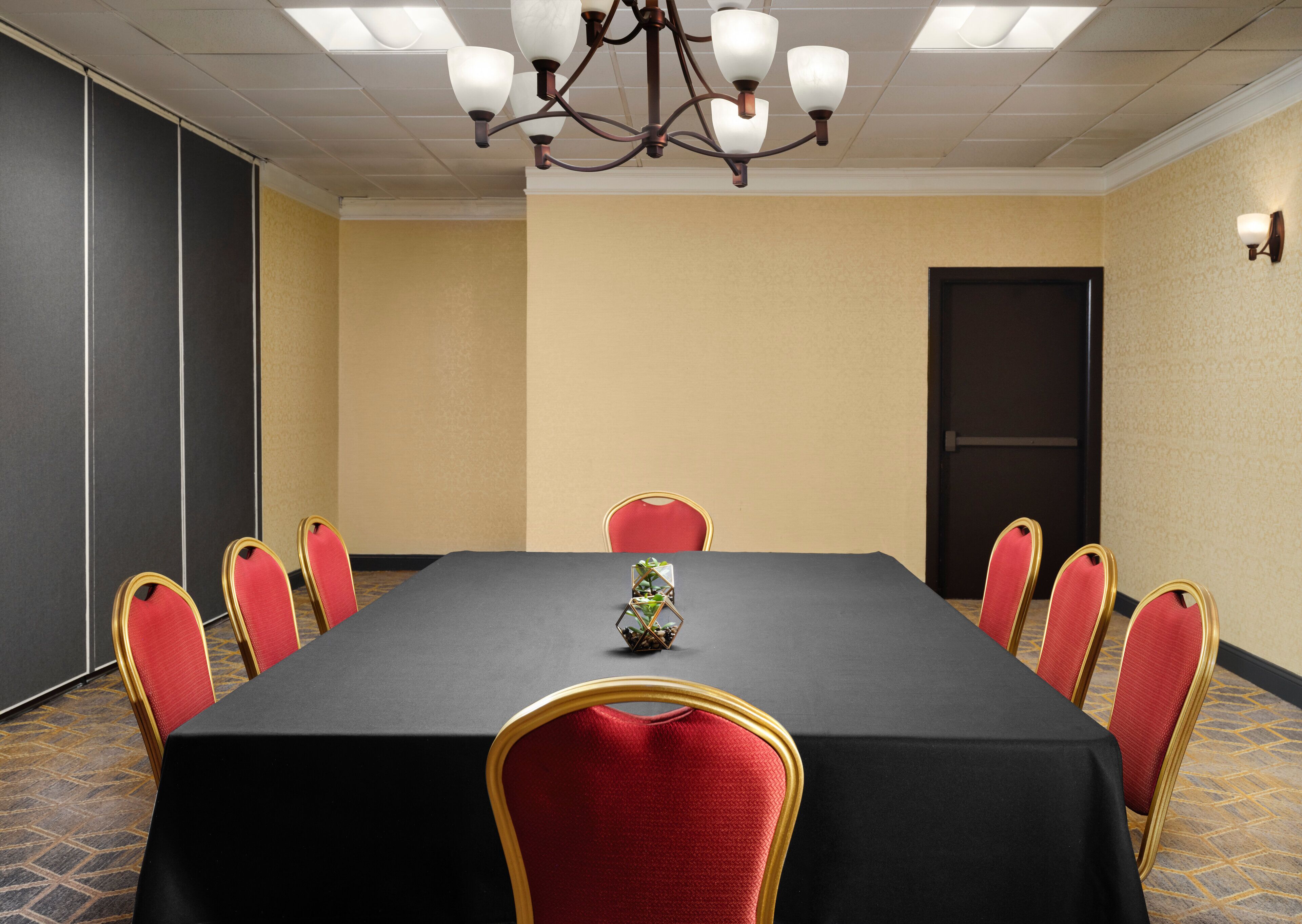 A conference room with a black table, red chairs, a chandelier, and a door.