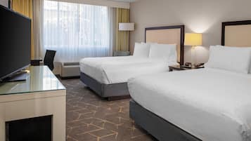 A hotel room with two beds, a desk with a TV, a lamp, and a clock on the nightstand.