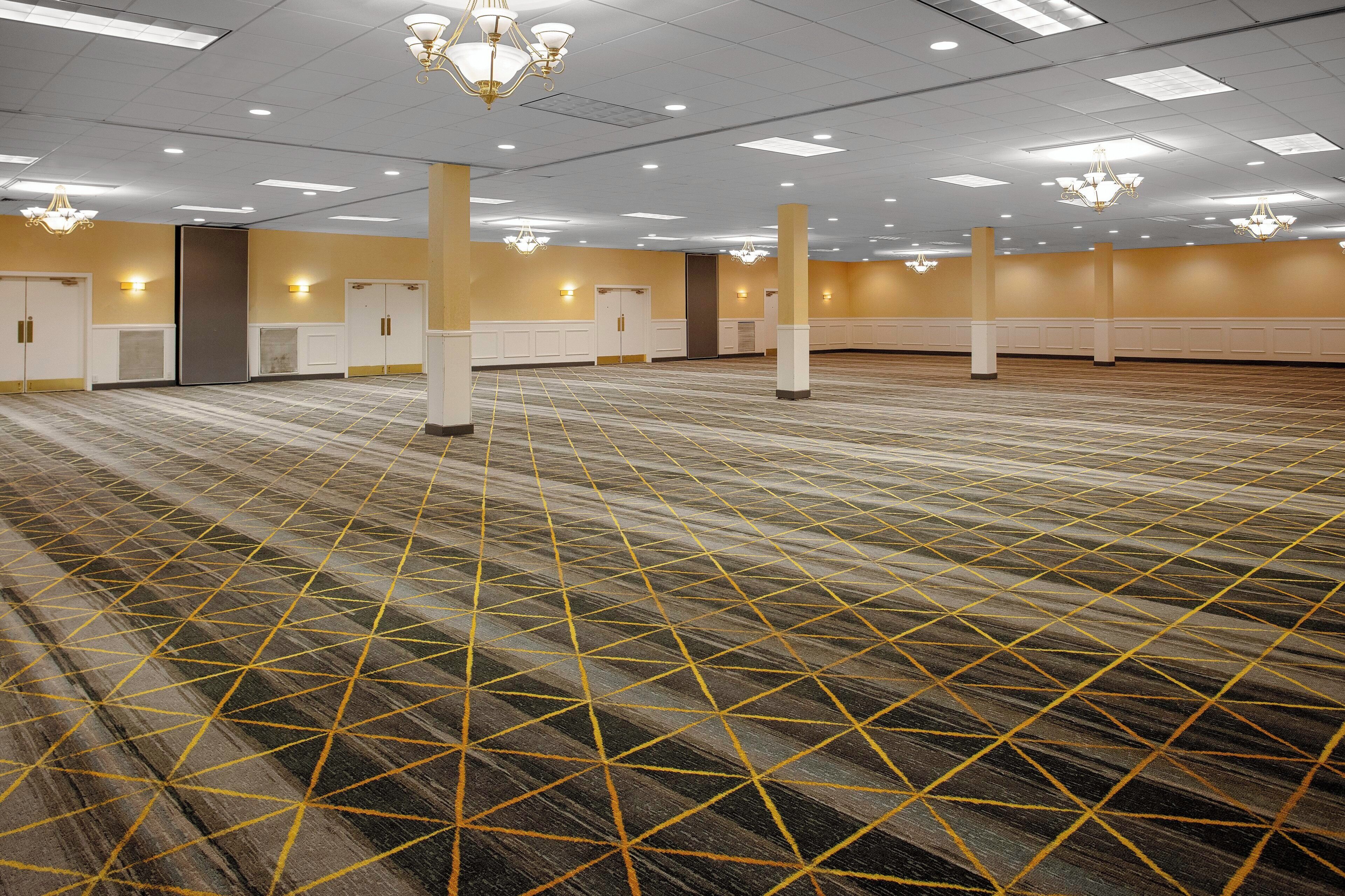 A large, empty conference room with a patterned carpet, white walls, and multiple doors.