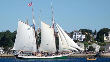 A large sailing ship with multiple masts and sails, docked at a harbor with a crowd of people on the shore.