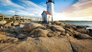 A lighthouse on a rocky shore with a wooden walkway leading to it.