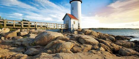 A lighthouse on a rocky shore with a wooden walkway leading to it.
