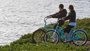 Two people riding a blue bicycle along a grassy path by the water.