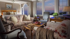 A spacious living room with a large bed, a sofa, and a chair. There is a chessboard on a table, and a view of the ocean through the windows. - Ocean House Hotel at Bass Rocks (Gloucester)