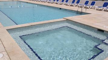 A swimming pool with clear blue water, a diving board, and a row of blue and white lounge chairs along the edge.
