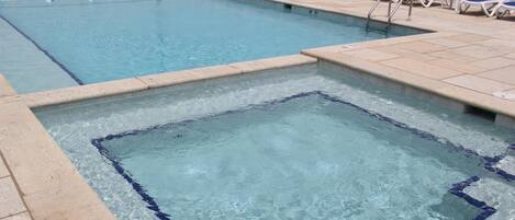 Una piscina con agua azul cristalina, un trampolín y una fila de sillones azules y blancos a lo largo del borde.