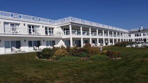 A white hotel with multiple balconies, outdoor seating, and a well-maintained garden.