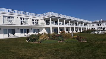 Um hotel branco com várias varandas, área de estar externa e um jardim bem cuidado.