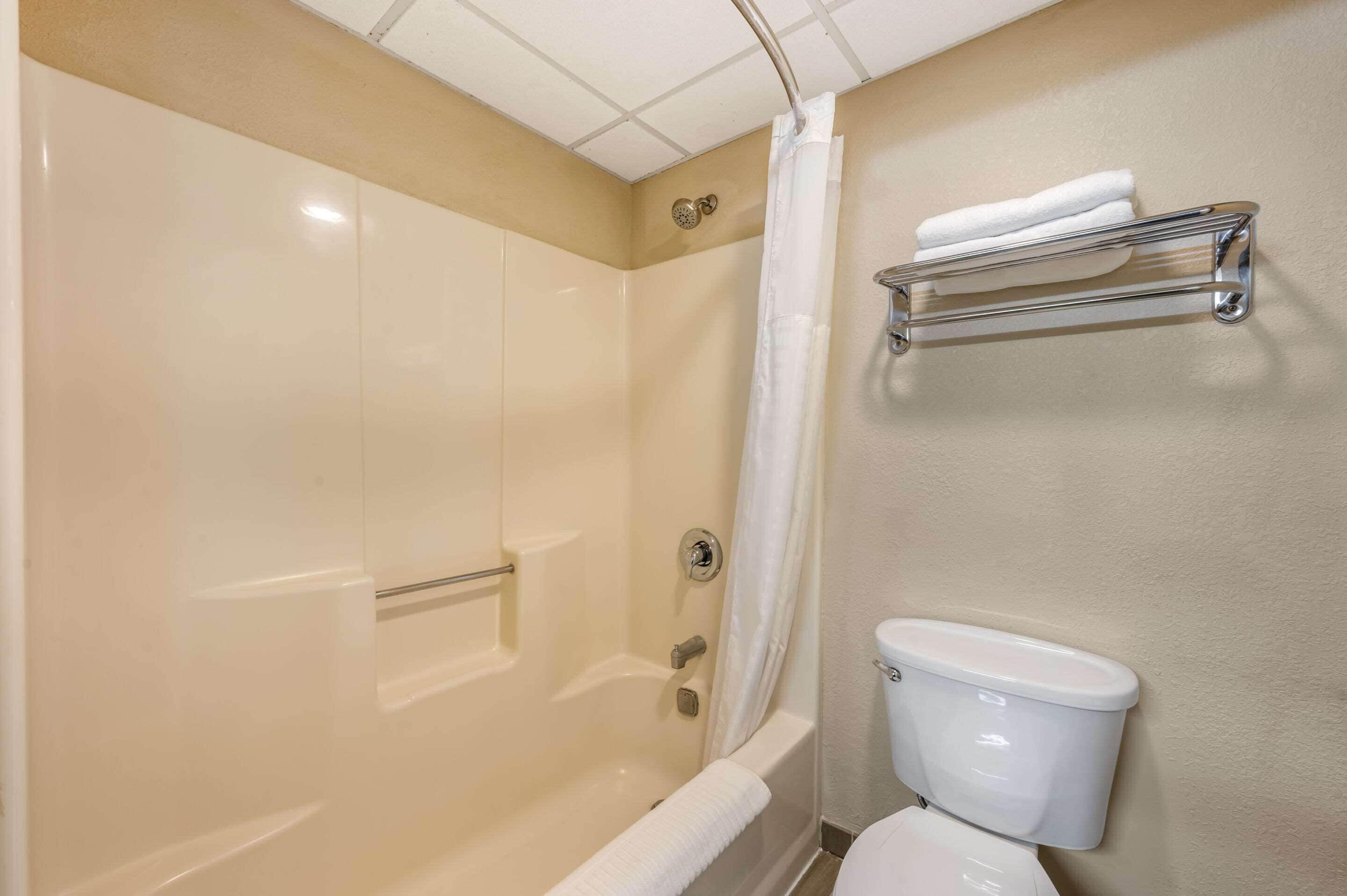 A bathroom with a bathtub, shower curtain, toilet, and a towel rack.