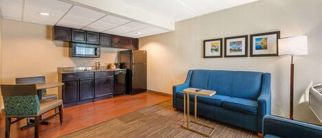 Un espacio habitable compacto con kitchenette, un sofá azul, una mesita y una silla.