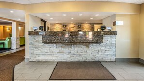 A reception area with a stone and granite counter, a reception desk, and a waiting area with green seating. - Comfort Inn & Suites East Hartford - Hartford (East Hartford)