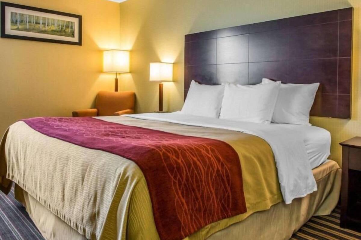 Hotellihuone, jossa on suuri sänky, kaksi yöpöytävalaisinta, sängynpääty ja seinällä oleva kehystetty kuva.