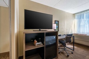 Habitación de hotel con una televisión de pantalla plana sobre un escritorio de madera, una silla, una lámpara y una ventana con cortinas.