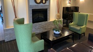A modern living room with a fireplace, green armchairs, a coffee table, and decorative mirrors. - Comfort Inn & Suites East Hartford - Hartford (East Hartford)
