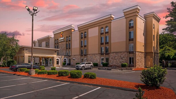 A hotel with a modern design, featuring a central entrance with a covered area, multiple floors, and a parking lot with red mulch landscaping. - Comfort Inn & Suites East Hartford - Hartford (East Hartford)