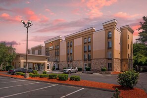 A hotel with a modern design, featuring a central entrance with a covered area, multiple floors, and a parking lot with red mulch landscaping.