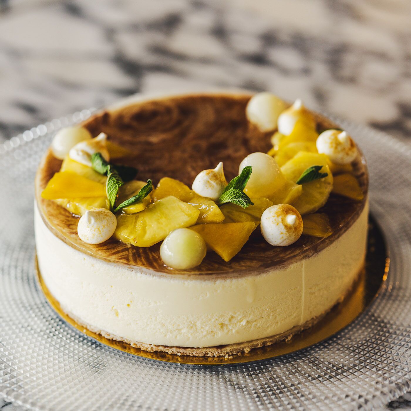 A round cheesecake with a crust, topped with fruit and small round white items, on a textured plate.