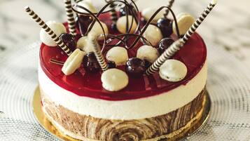 A layered cake with a red jelly topping, white cream layer, and a chocolate base, decorated with cherries and chocolate curls.