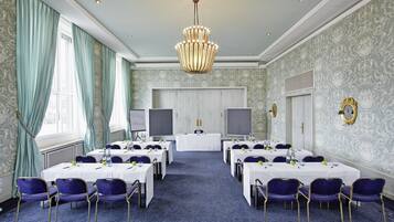 A conference room with tables, chairs, a chandelier, and patterned wallpaper.