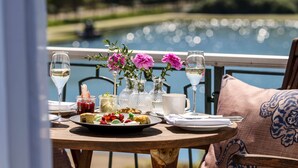 Mesa servida con comida, vasos y flores, con vista al lago.