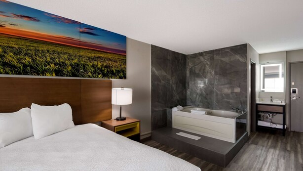 Ein modernes Hotelzimmer mit einem großen Bett, einem Nachttisch, einem Wandbild, einem Marmorbad und einem Holzboden.