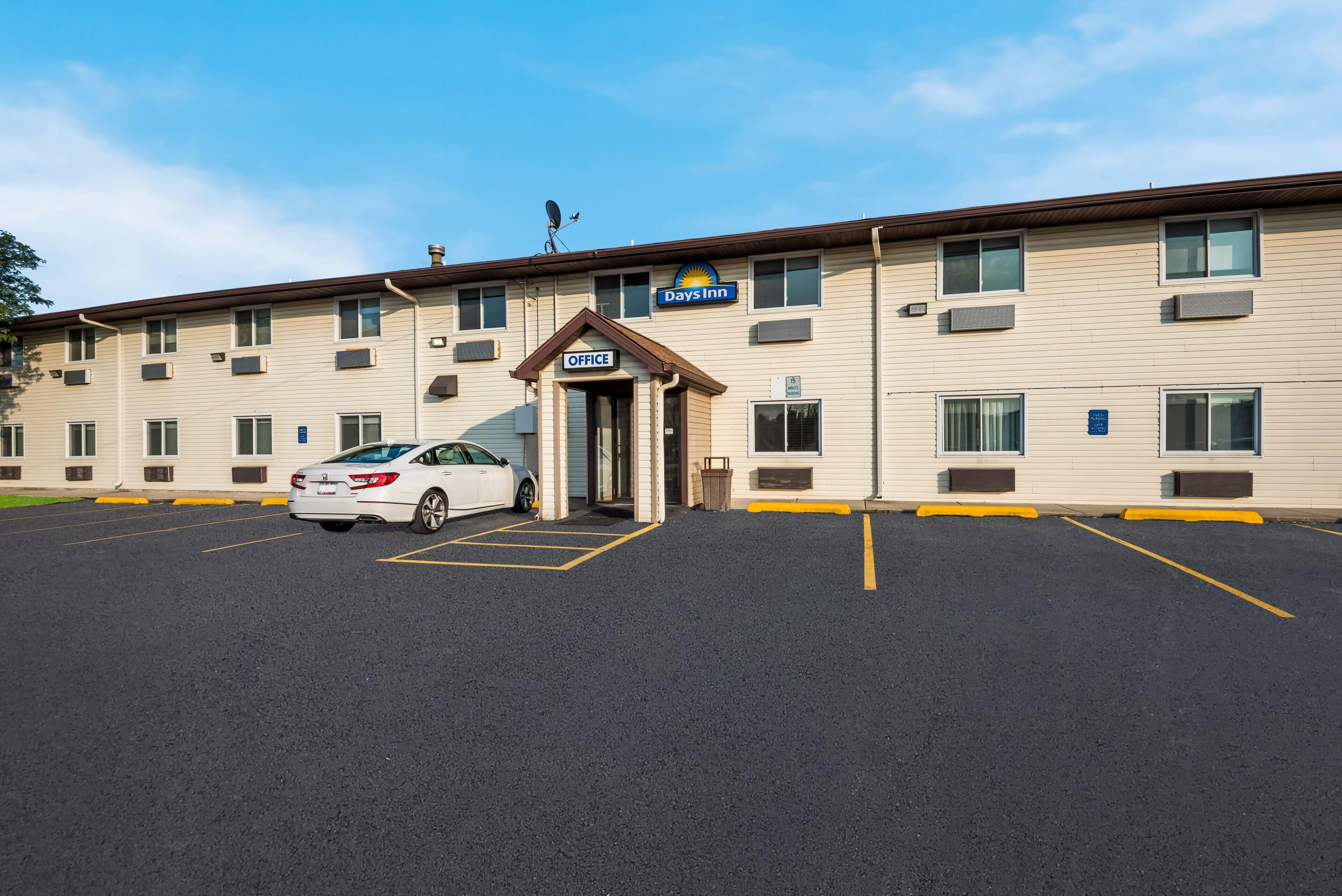 A Days Inn with a parking lot, a white car parked in front, and a clear blue sky.