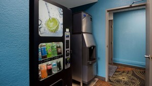 Ein Getränkeautomat mit Zitronenlimetten-Design, ein Kühlschrank und eine Tür zu einem Raum mit blauer Wand und gemustertem Teppich.
