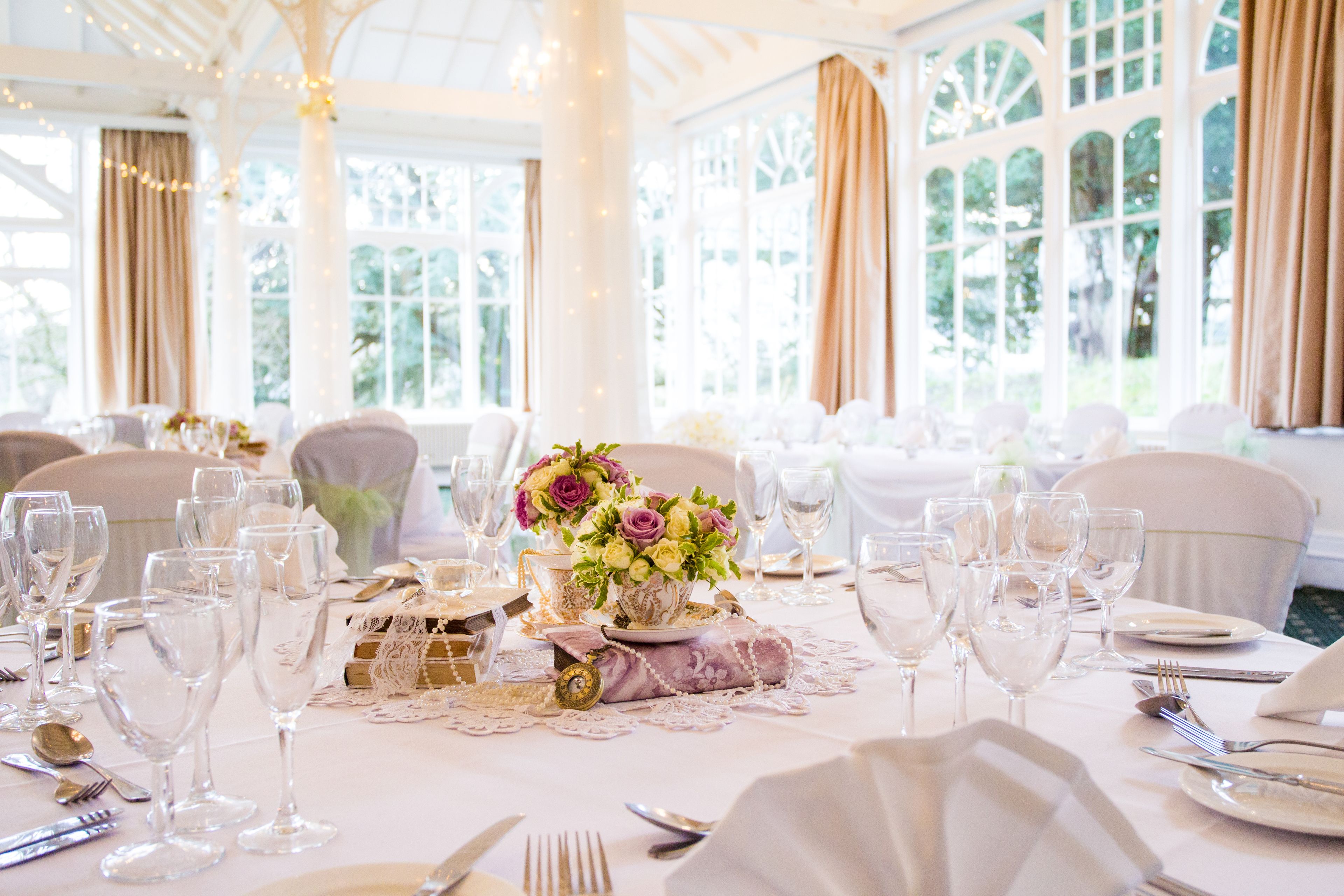 Une salle de banquet avec des tables rondes dressées pour un événement formel, agrémentée de verres transparents et de compositions florales.